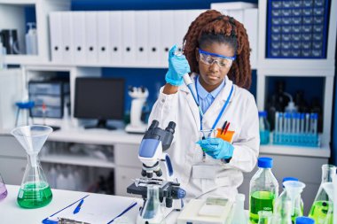 Laboratuvarda test tüpüne sıvı döken Afrikalı Amerikalı kadın bilim adamı.