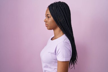 African american woman with braids standing over pink background looking to side, relax profile pose with natural face and confident smile. 