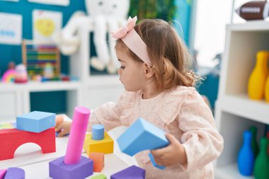 Anaokulunda duran sevimli sarışın çocuk inşaat bloklarıyla oynuyor.