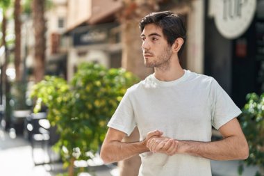 Latin kökenli genç adam ciddi bir ifadeyle sokağa bakıyor.
