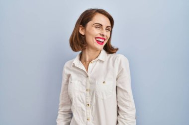 Young beautiful woman standing casual over blue background looking away to side with smile on face, natural expression. laughing confident. 