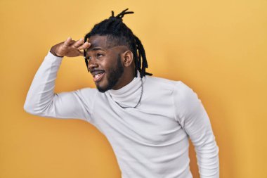 Sarı arka planda balıkçı yaka kazak giyen Afrikalı adam çok mutlu ve tebessüm ediyor. arama kavramı. 