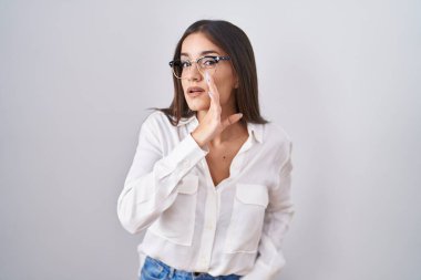 Young brunette woman wearing glasses hand on mouth telling secret rumor, whispering malicious talk conversation 