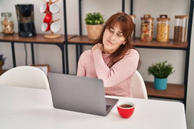 Boyun ağrısı çeken orta yaşlı bir kadın evde masada oturuyor.