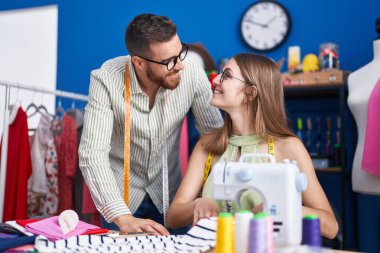 Man and woman tailors smiling confident using sewing machine at clothing factory