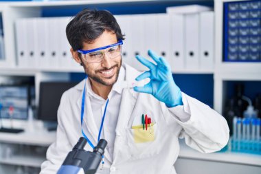 Young hispanic man scientist smiling confident holding sample at laboratory