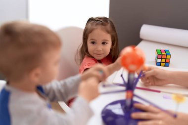 Adorable girl and boy sitting on table learning of planets at kindergarten