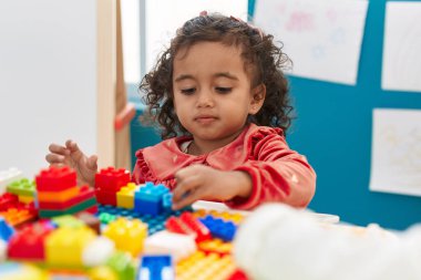 Anaokulundaki masada oturan, inşaat bloklarıyla oynayan sevimli İspanyol kız.