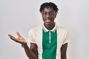 African man with dreadlocks standing over isolated background smiling cheerful presenting and pointing with palm of hand looking at the camera. 