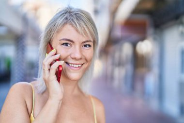 Genç sarışın kadın gülümsüyor. Kendine güveni tam. Akıllı telefondan konuşuyor.