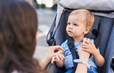 Anne ve oğlu sokakta bebek arabasında otururken kendinden emin bir şekilde gülümsüyor.