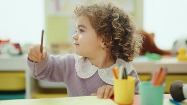Adorable hispanic girl preschool student sitting on table drawing on paper at kindergarten