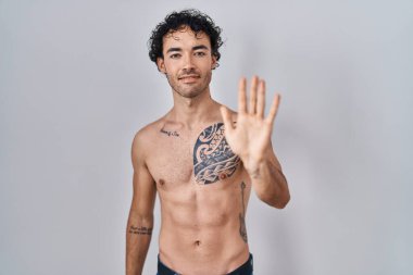 Hispanic man standing shirtless showing and pointing up with fingers number five while smiling confident and happy. 