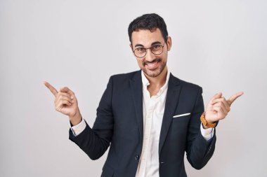 Handsome business hispanic man standing over white background smiling confident pointing with fingers to different directions. copy space for advertisement 