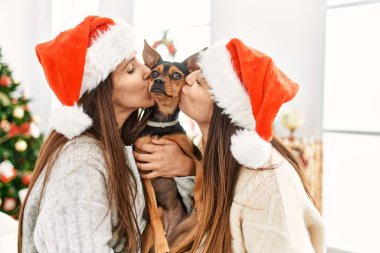 Evde Noel ağacının yanında öpüşen ve sarılan iki kadın.