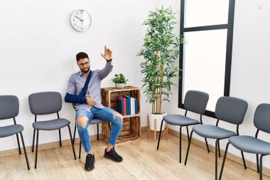 Kol askısı ve parmağıyla kliniğin bekleme odasında oturan genç Arap adam acı çekiyor.