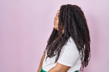 Plus size hispanic woman standing over pink background looking to side, relax profile pose with natural face and confident smile. 