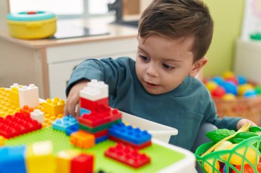 Anaokulundaki masada oturan, inşaat bloklarıyla oynayan sevimli İspanyol çocuk.