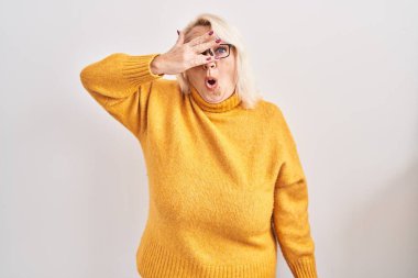 Orta yaşlı, beyaz gözlüklü bir kadın. Arka planda dikiliyor. Şoka girip yüzünü ve gözlerini eliyle kapatıyor.. 