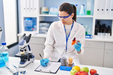 Young beautiful hispanic woman scientist weighing food writing report at street