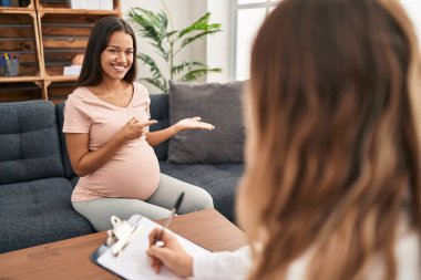Young pregnant woman at therapy session amazed and smiling to the camera while presenting with hand and pointing with finger. 
