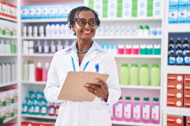 Middle age african american woman pharmacist writing on document at pharmacy