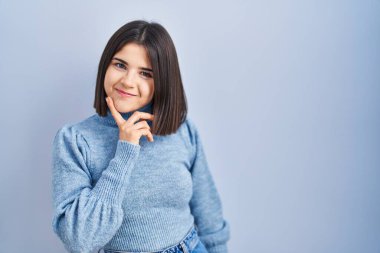 Mavi arka planda duran Latin kökenli genç bir kadın parmak çenesinde şüpheye yoğunlaşmıştı. 