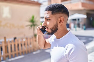 Sokakta ciddi bir ifadeyle akıllı telefondan konuşan genç latin adam.