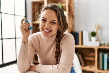 Evdeki masada oturan, astım spreyi kullanan genç, güzel İspanyol kadın.