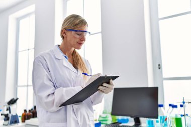 Laboratuvarda panoya yazan bilim adamı üniforması giyen genç sarışın kadın.