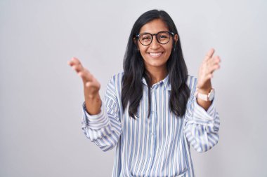 Young hispanic woman wearing glasses smiling cheerful offering hands giving assistance and acceptance. 