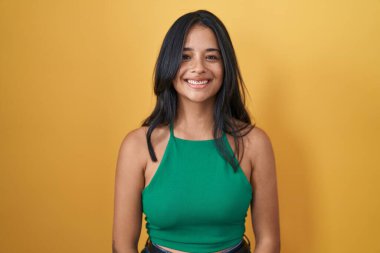 Brunette woman standing over yellow background with a happy and cool smile on face. lucky person. 
