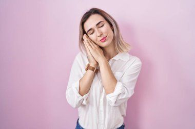 Genç, güzel bir kadın pembe arka planda ayakta uyur. Yorgun düşler kurar, ellerle poz verir ve gözleri kapalı gülümserdi.. 