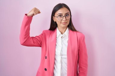 Young hispanic woman wearing business clothes and glasses strong person showing arm muscle, confident and proud of power 