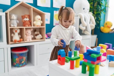Adorable blonde girl playing with construction blocks standing at kindergarten