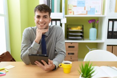 Young hispanic man business worker using touchpad drinking coffee at office