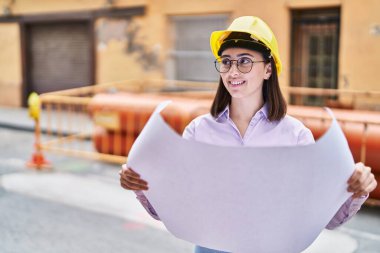 Young hispanic woman architect reading plans at street