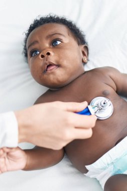 African american baby having medical examination lying on bed at bedroom