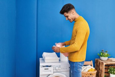 Genç İspanyol adam gülümsüyor. Çamaşırhaneye deterjan döküyor.