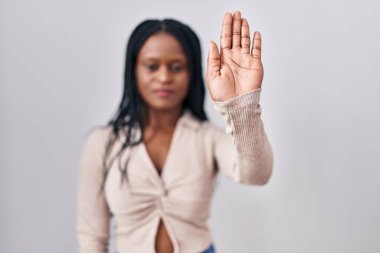 African woman with braids standing over white background doing stop sing with palm of the hand. warning expression with negative and serious gesture on the face. 