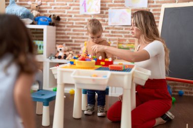 Teacher and toddler playing with construction blocks sitting on table at kindergarten