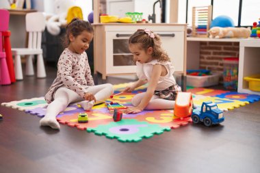 Two kids playing xylophone sitting on floor at kindergarten