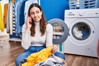 Young beautiful hispanic woman smiling confident talking on smartphone at laundry room