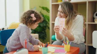 Teacher and toddler sitting on table having language lesson at kindergarten