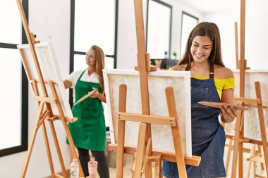 Anne ve kızı resim stüdyosunda kendine güvenen bir şekilde gülümsüyor.