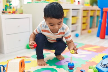 Anaokulunda yerde oturmuş halkalarla oynayan sevimli İspanyol çocuk.