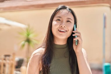 Genç Çinli kadın gülümsüyor caddede akıllı telefondan konuşuyor.