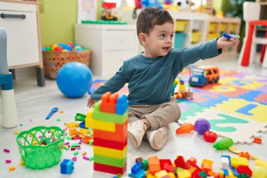 Adorable hispanic boy playing with construction blocks sitting on floor at kindergarten