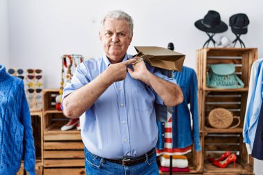Senior man with grey hair holding shopping bags at retail shop smiling happy pointing with hand and finger 