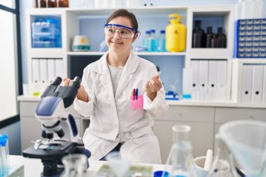 Hispanic girl with down syndrome working at scientist laboratory doing money gesture with hands, asking for salary payment, millionaire business 